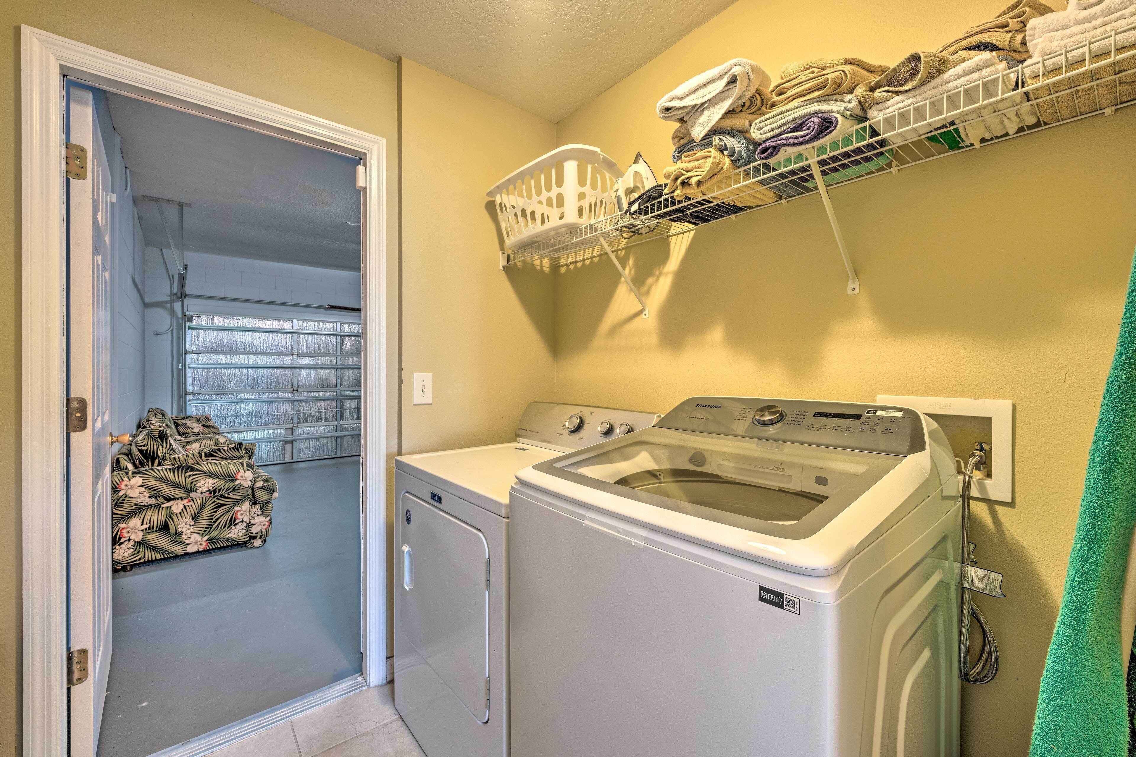 A laundry room with a front-loading washer and dryer, a drying rack, and a basket of folded towels.