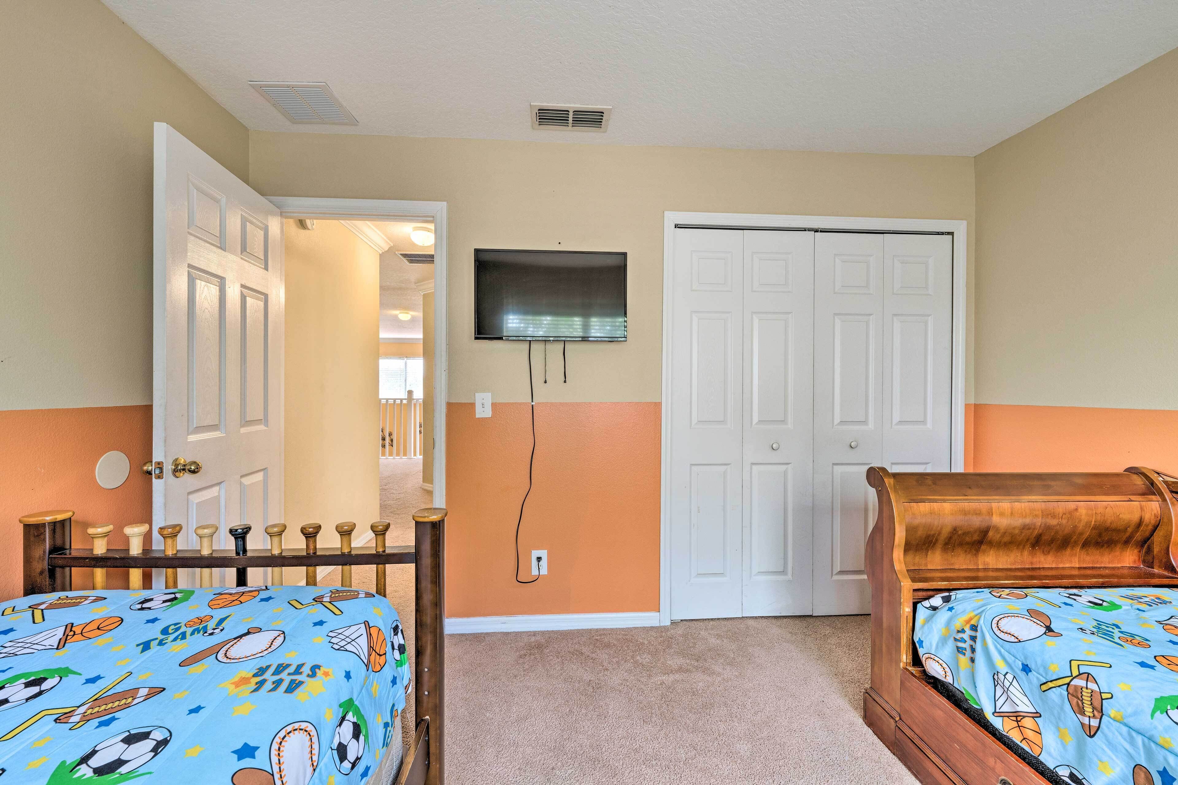 A bedroom with two beds, a TV mounted on the wall, and a door leading to another room.
