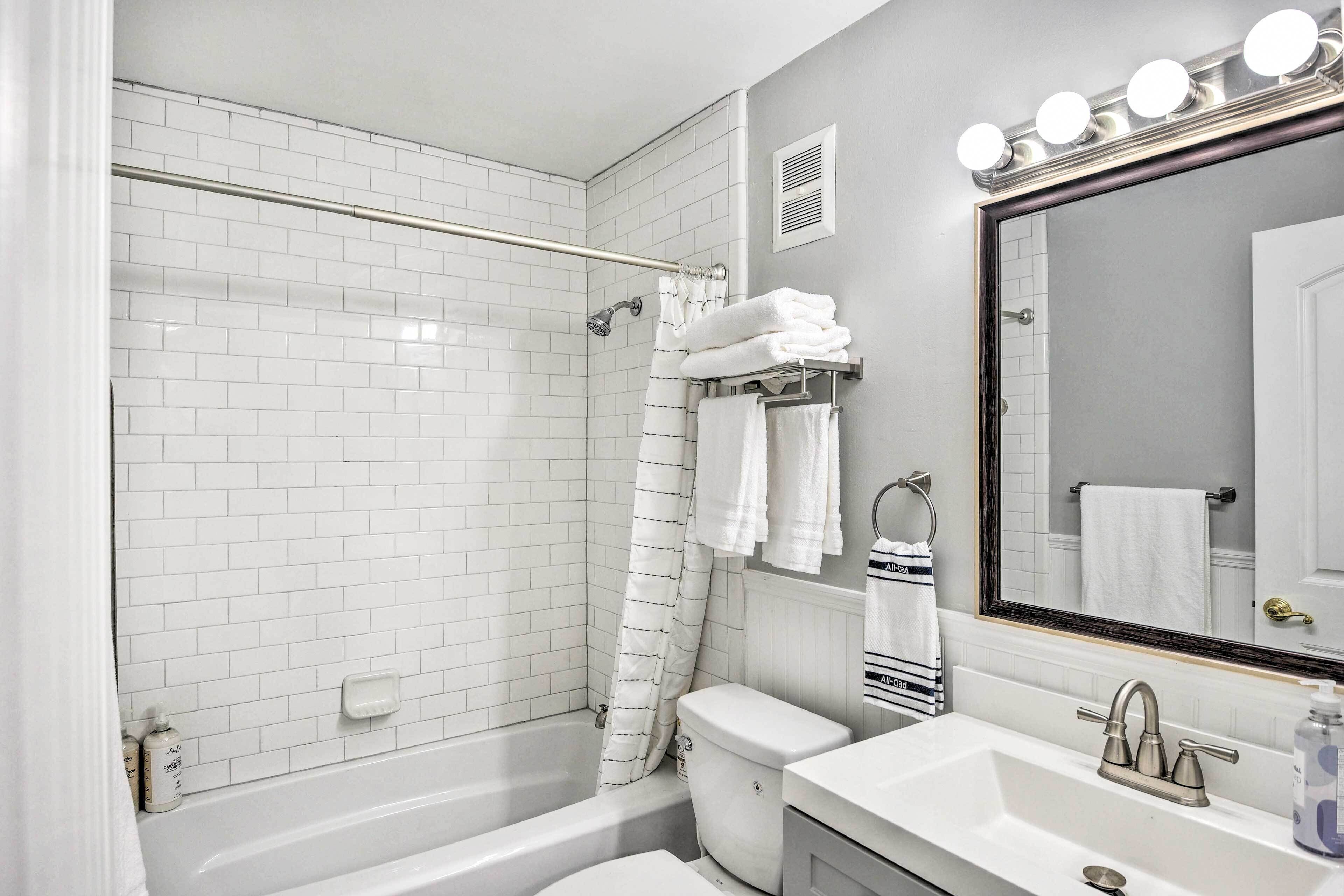 A bathroom with white subway tiles, a bathtub, a toilet, a sink with a mirror, and a shower curtain.