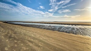 Ein Strand mit Fußabdrücken und einer weiten Sandfläche, die zum Wasser führt.
