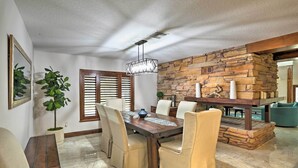 A dining area with a wooden table, beige chairs, a potted plant, and a stone accent wall. - The Peacock Farm Largo Home + Outdoor Oasis! (Seminole)