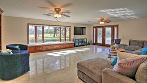 A spacious living room with a large window, a ceiling fan, and a flat-screen TV. - The Peacock Farm Largo Home + Outdoor Oasis! (Seminole)