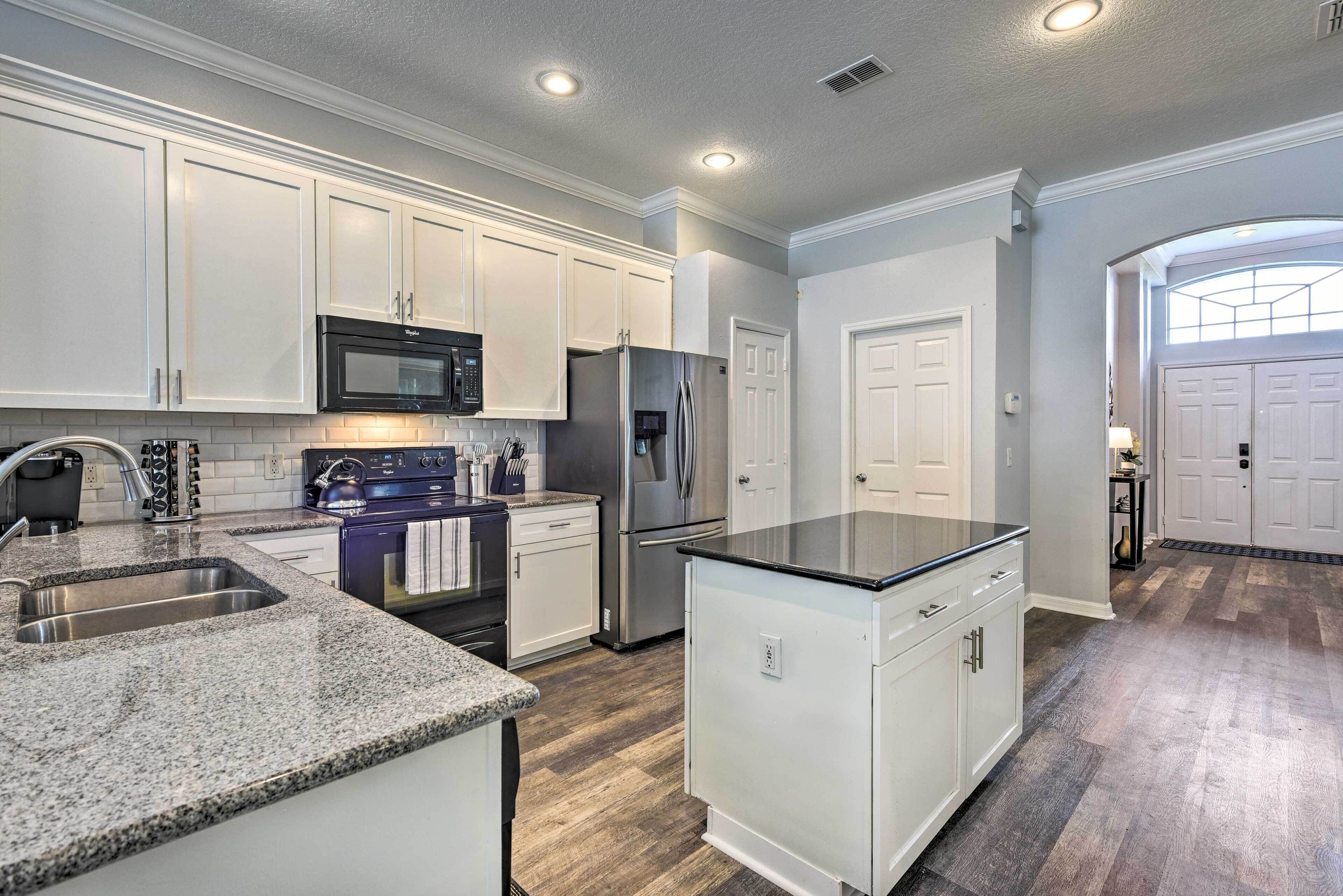 A kitchen with white cabinets, a granite countertop, stainless steel appliances, and a wooden floor.