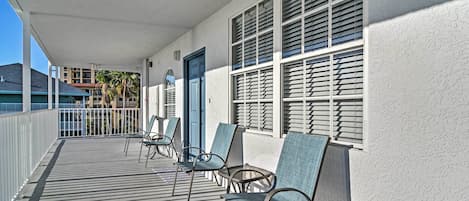 Un espace extérieur abrité, avec une rangée de chaises, une porte et des fenêtres équipées de volets.