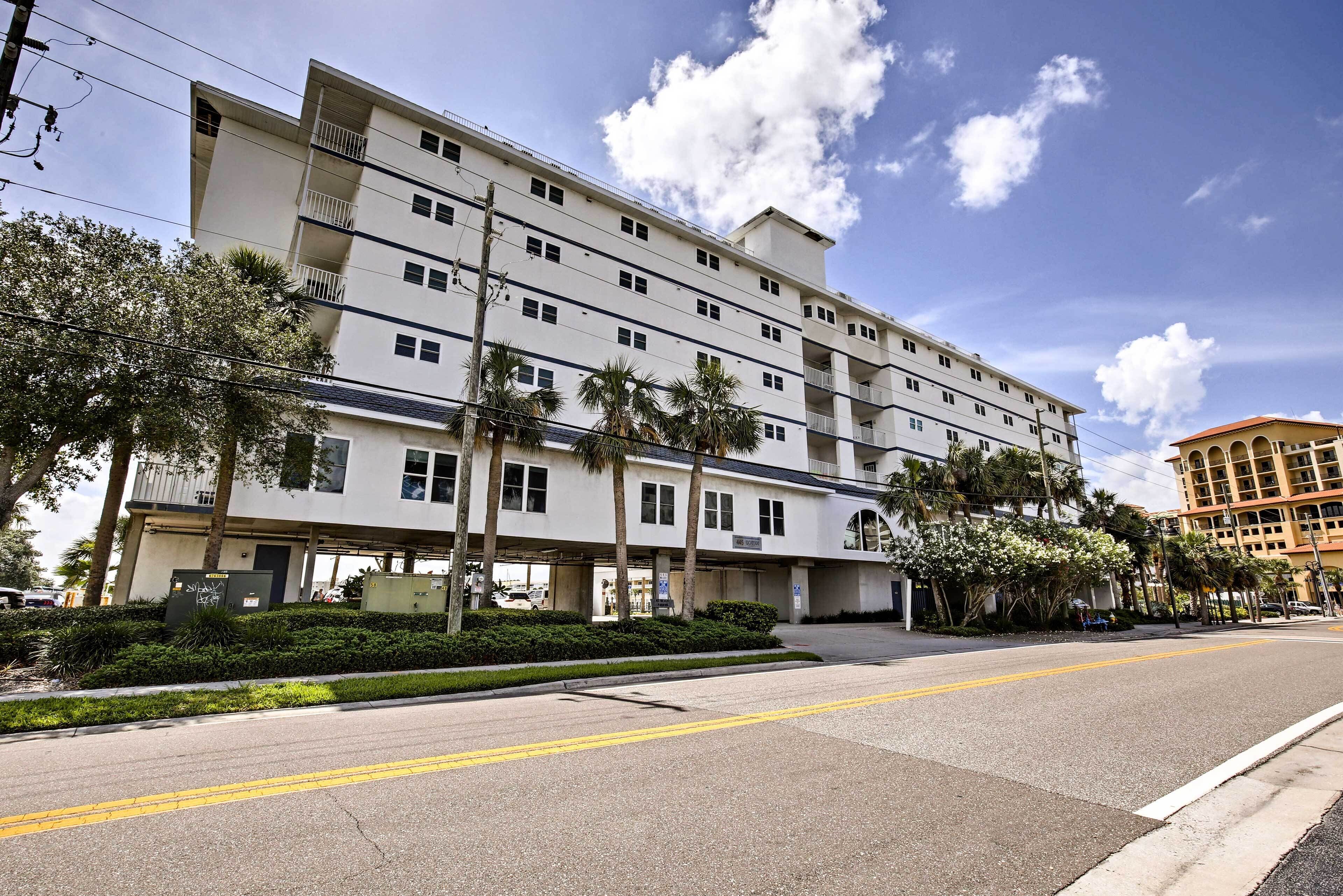 A multi-story hotel with balconies, a parking area, and palm trees.