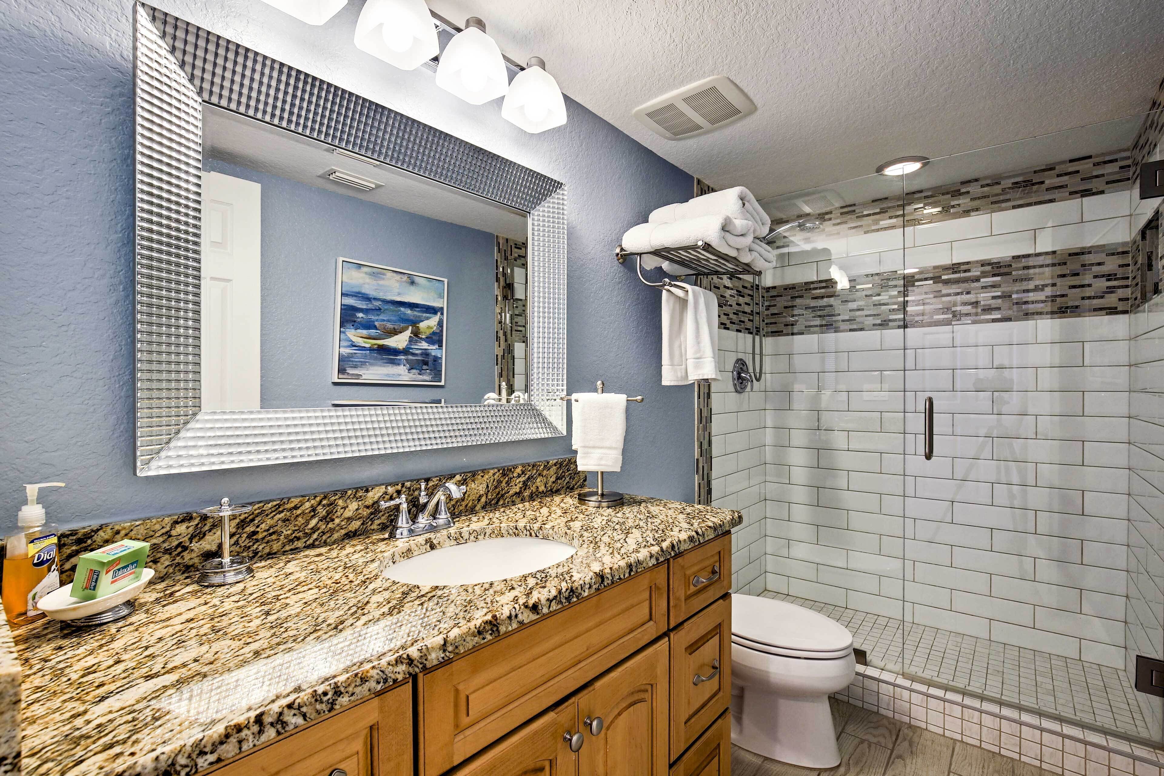 Une salle de bain avec un lavabo sur un plan de travail en granit, un grand miroir, un tableau et une douche avec une porte en verre.