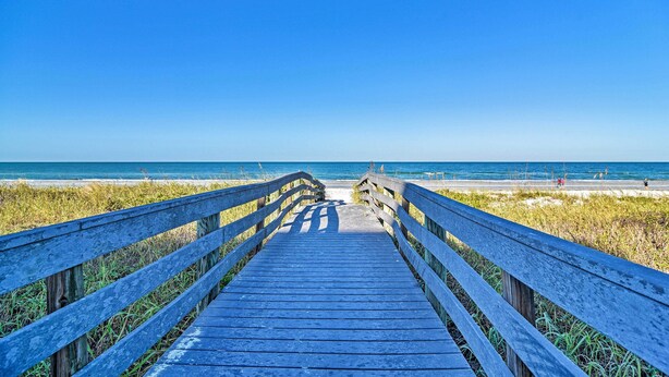 Een houten looppad dat naar een strand leidt, onder heldere luchten.
