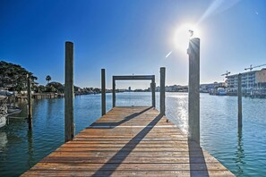Une jetée en bois s  ’étendant sur une étendue d’eau calme, avec un ciel dégagé au-dessus et des bâtiments en arrière-plan.