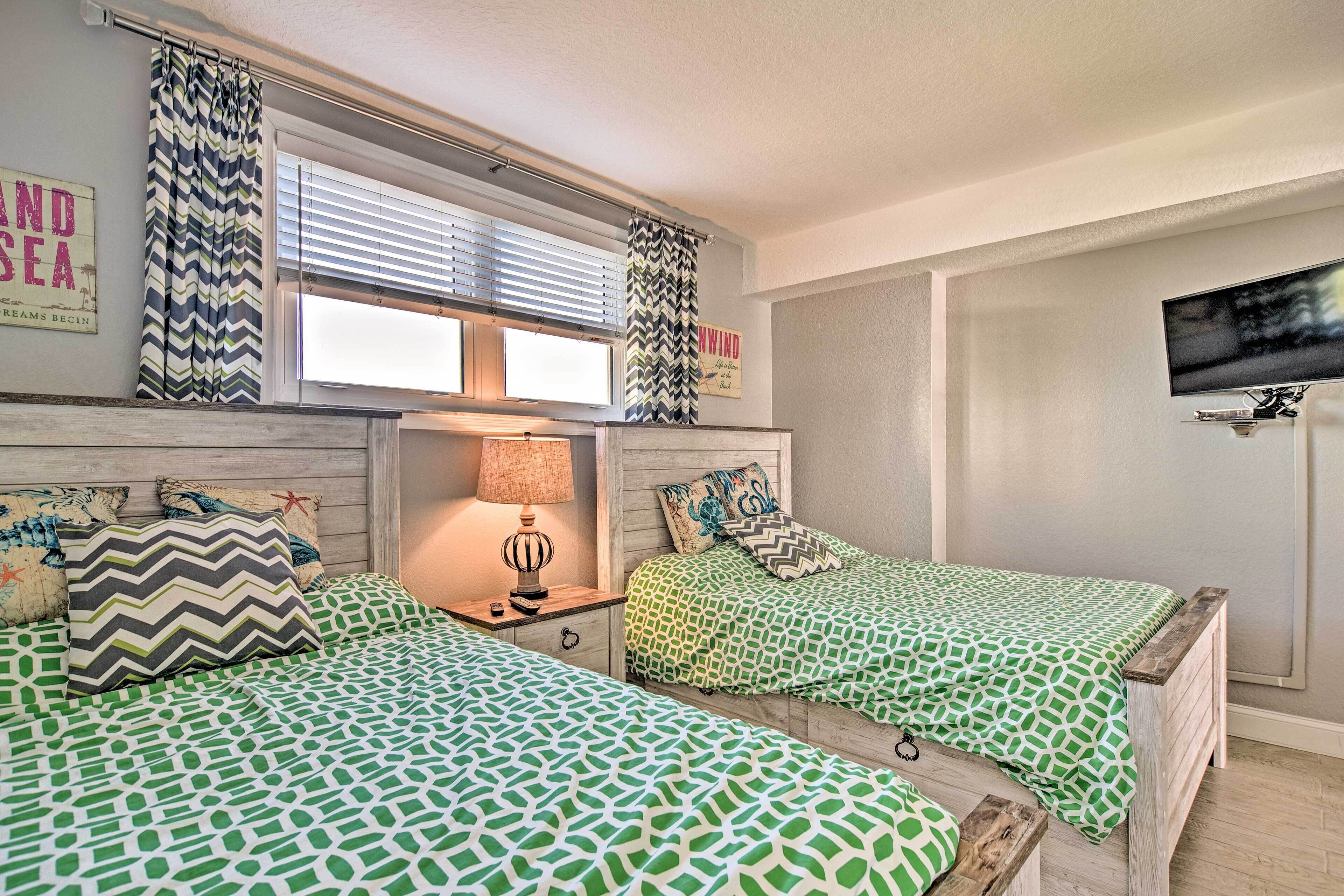 Un dormitorio con dos camas, una mesita de noche, una lámpara, un televisor y una ventana con cortinas.