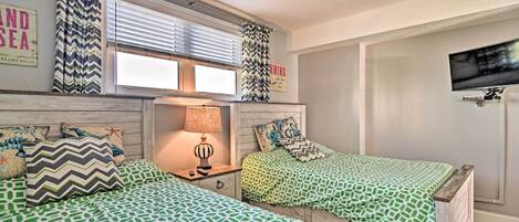 Un dormitorio con dos camas, una mesita de noche, una lámpara, un televisor y una ventana con cortinas.