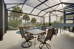 A covered outdoor area with a pool table, chairs, and a view of palm trees and houses. - Tropical Bayfront Escape w/ Heated Pool & Dock! (Englewood)