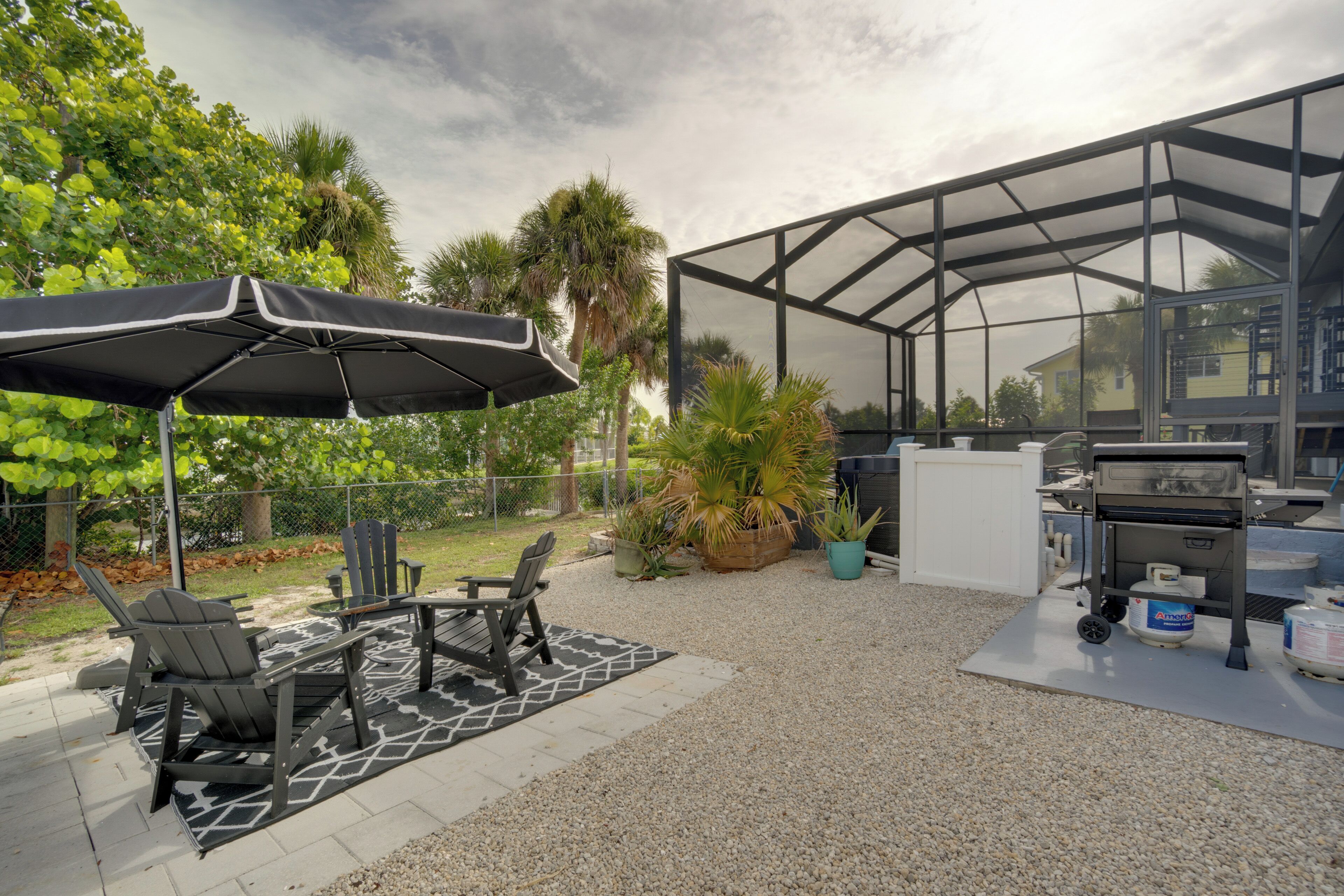 An outdoor patio with a grill, chairs, and an umbrella.