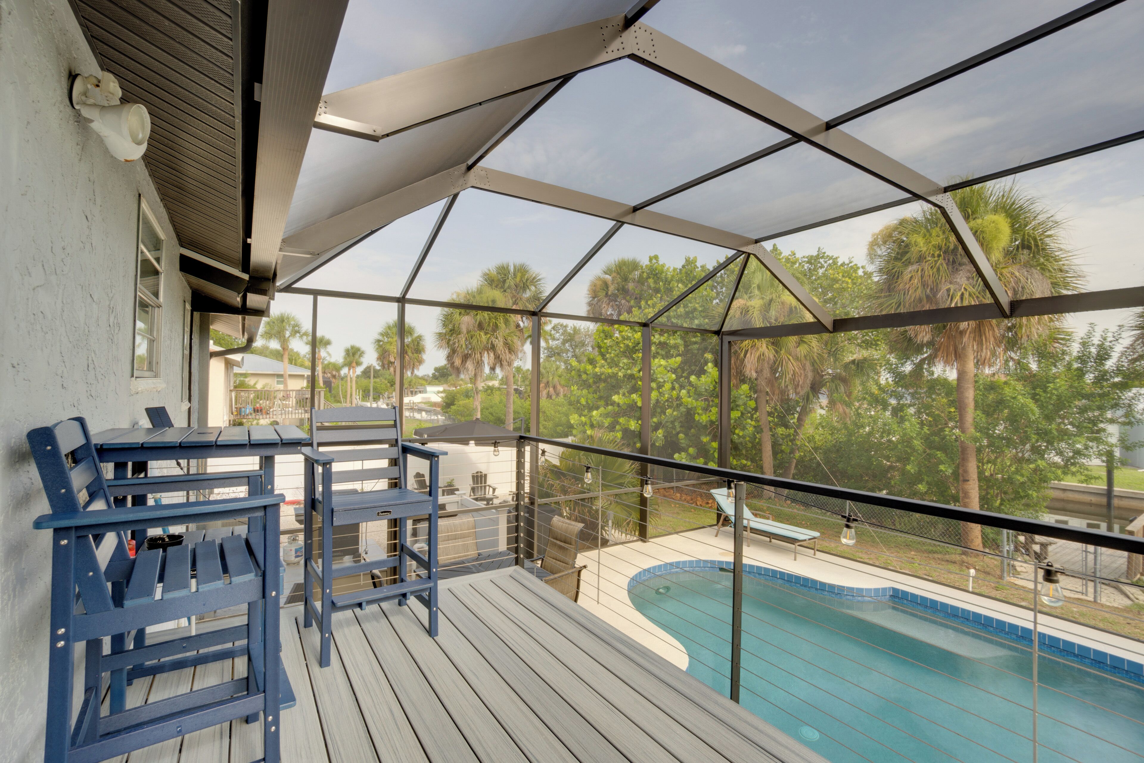 Un espacio al aire libre techado con piscina, sillas azules y vistas a palmeras.