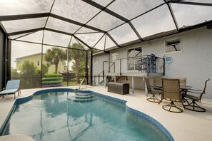 An indoor swimming pool with a glass ceiling, a patio area with outdoor furniture, and a view of a residential neighborhood. - Tropical Bayfront Escape w/ Heated Pool & Dock! (Englewood)
