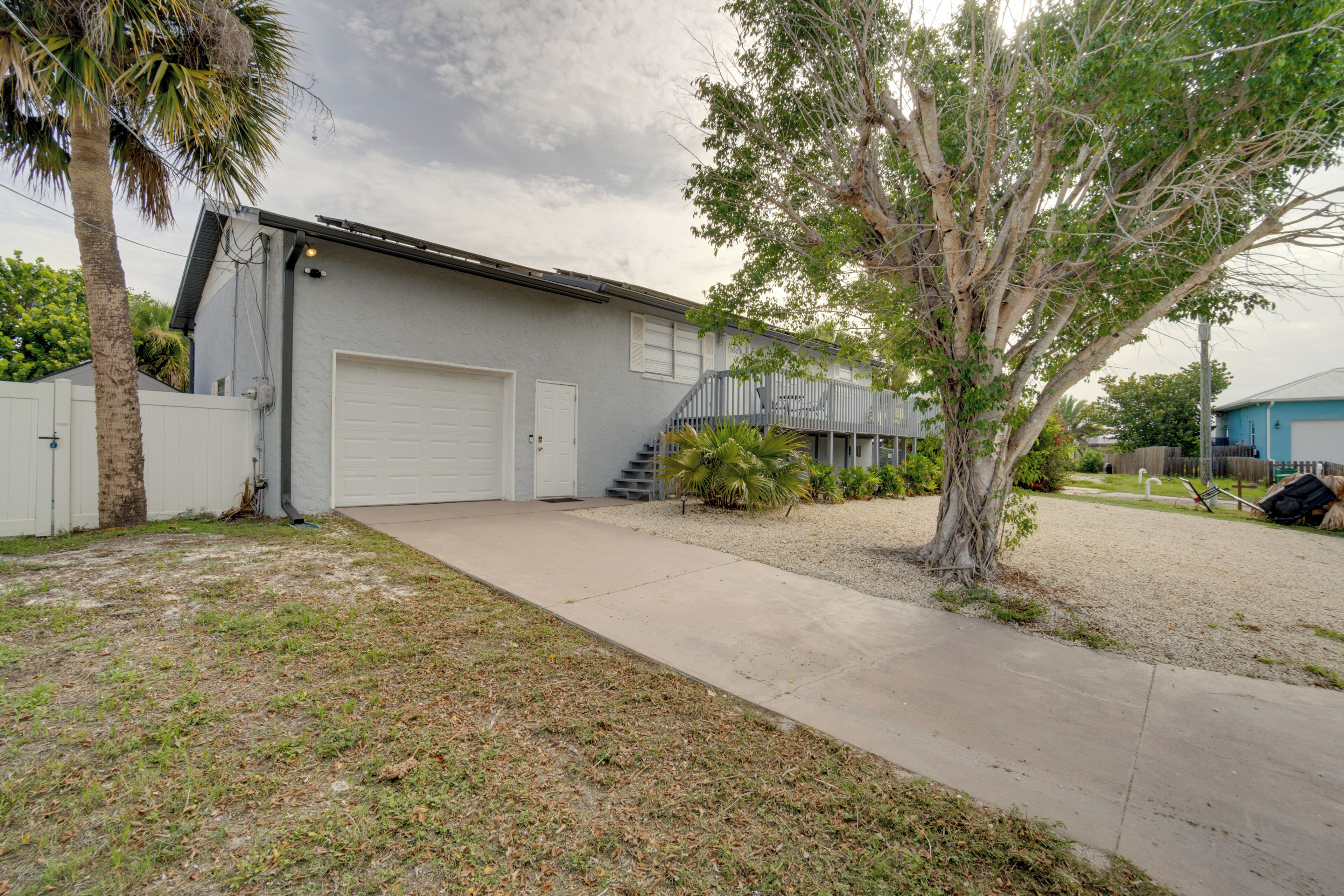 A residential garage with a white door, a concrete driveway, and a tree in the foreground.