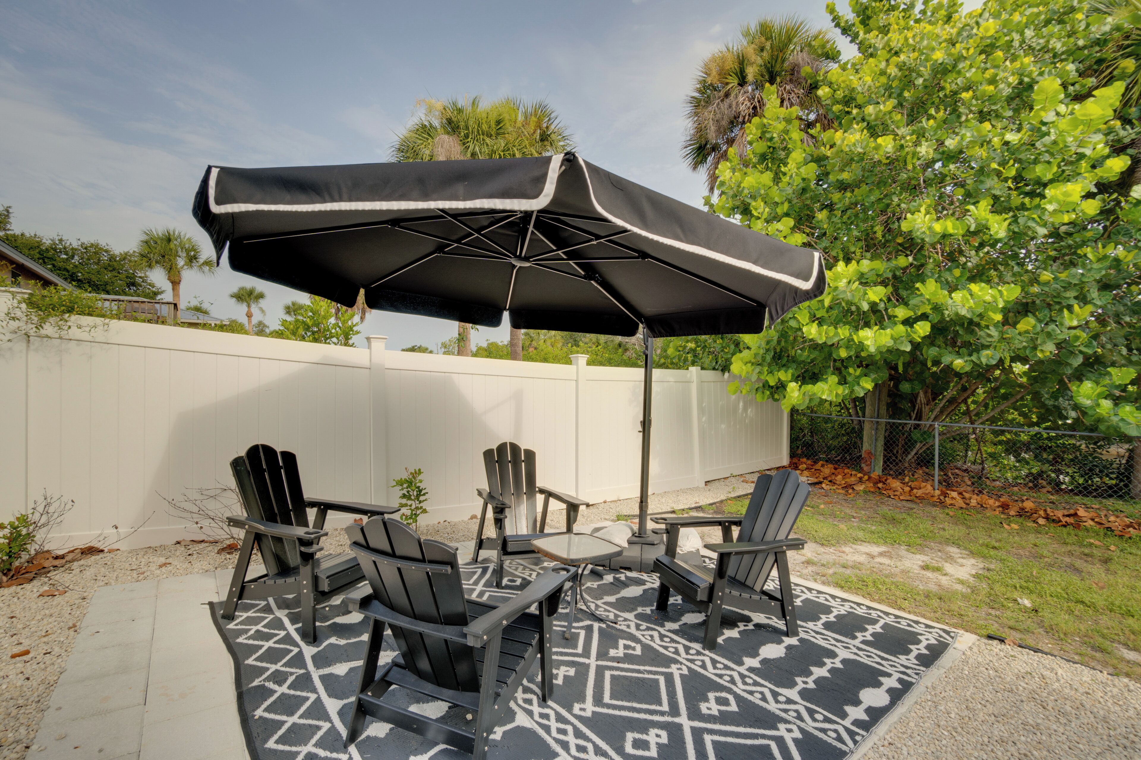 An outdoor patio with a table and four chairs, a patterned rug, and a large umbrella.
