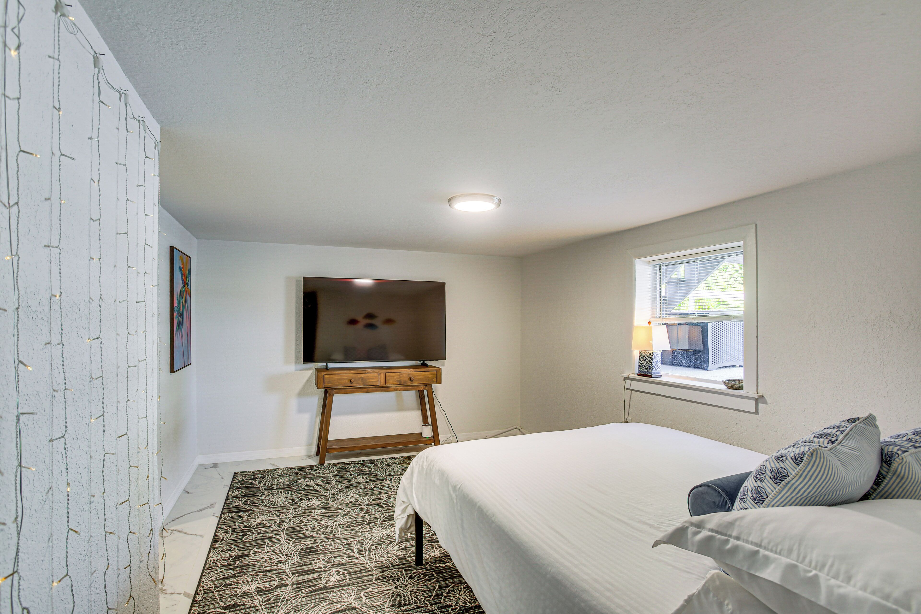 Une chambre à coucher avec un lit, un téléviseur posé sur un meuble, une fenêtre et un tapis à motifs.