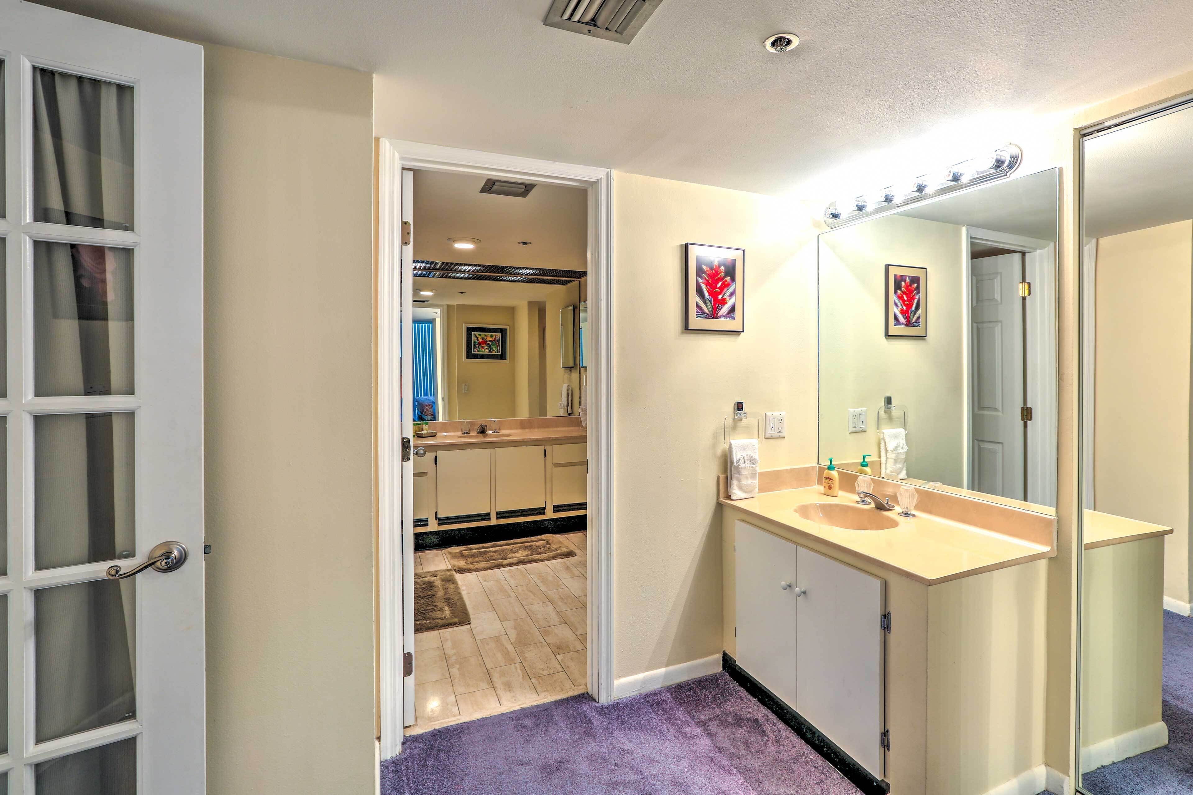 A bathroom with a vanity, mirror, and a door leading to a hallway.