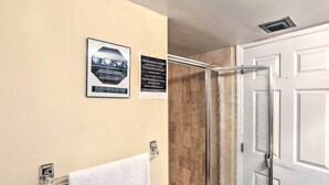 A bathroom with a white towel rack, a shower with a glass door, and two informational posters on the wall. - Bayfront Miami Condo w/ Resort Perks & Ocean Views (Miami)