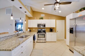 A kitchen with white cabinets, a stainless steel refrigerator, a microwave, and an oven. - Pool & Outdoor Bar: Cape Coral Home (Cape Coral)