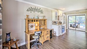 Un bureau à domicile avec un bureau, une chaise et des étagères en bois, un coin repas avec une table et des chaises, et une vue sur le jardin à travers des portes vitrées.