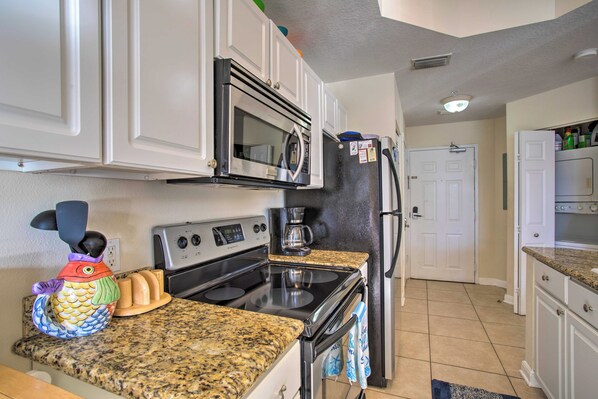 Una cocina con gabinetes blancos, estufa de acero inoxidable, microondas y refrigerador.