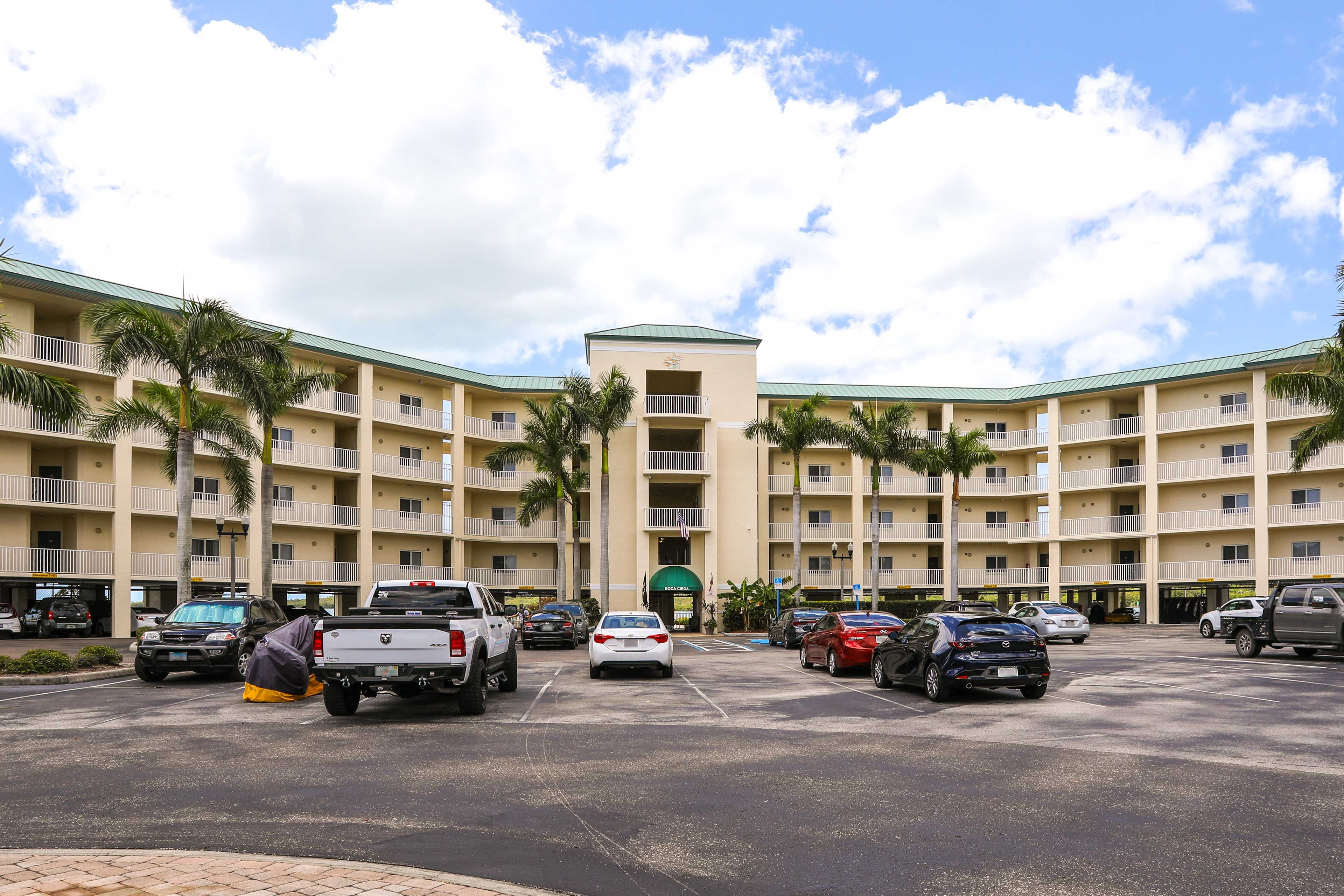 A multi-story hotel with a central entrance, parking lot, and palm trees.