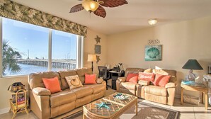 A living room with a large window, a ceiling fan, a sofa, a chair, a coffee table, and a desk with a lamp. - Best Views in St Pete for Dolphin Viewing (St. Petersburg)