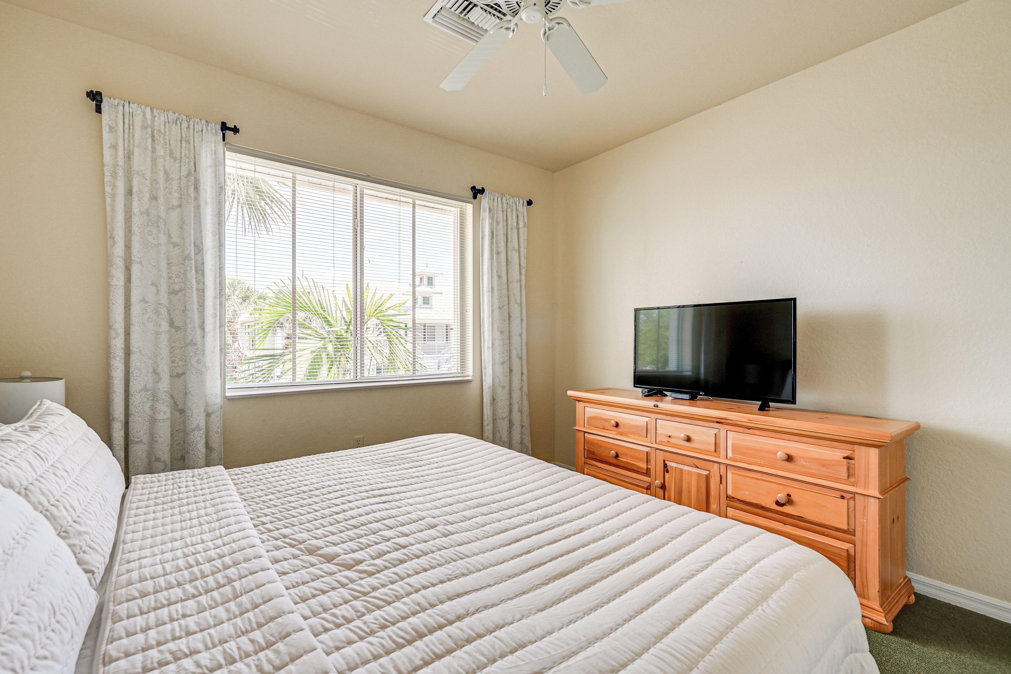 A hotel room with a large bed, a wooden dresser, a television, and a window with curtains.