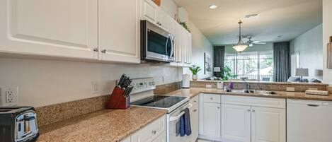 A modern kitchen with white cabinetry, granite countertops, a built-in microwave, and a stainless steel range.