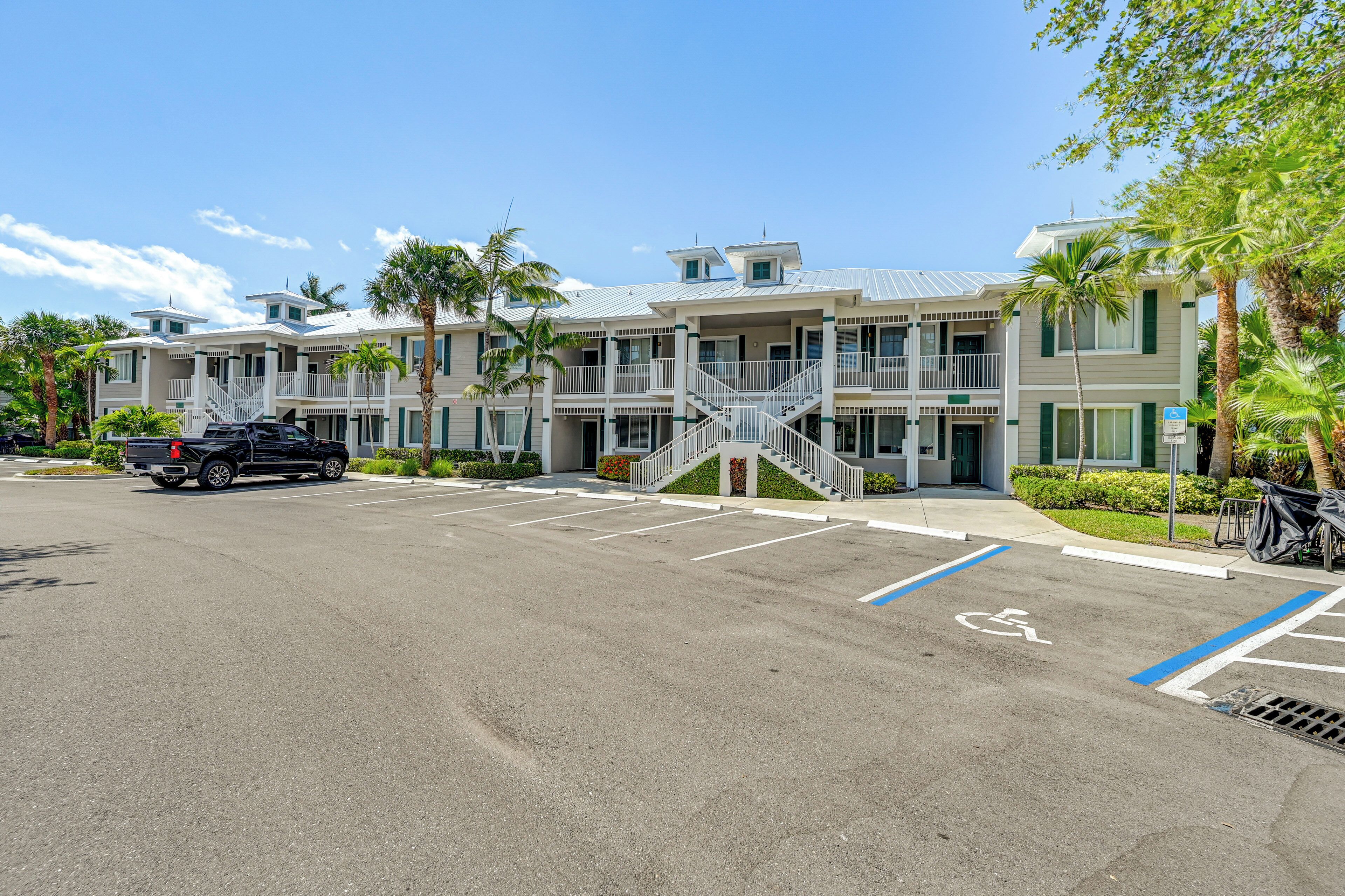 A multi-story hotel with a parking lot, wheelchair-accessible spaces, and a staircase leading to the entrance.