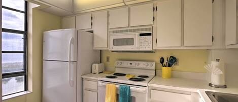Una cocina con gabinetes blancos, un refrigerador, un microondas, una estufa y un fregadero.