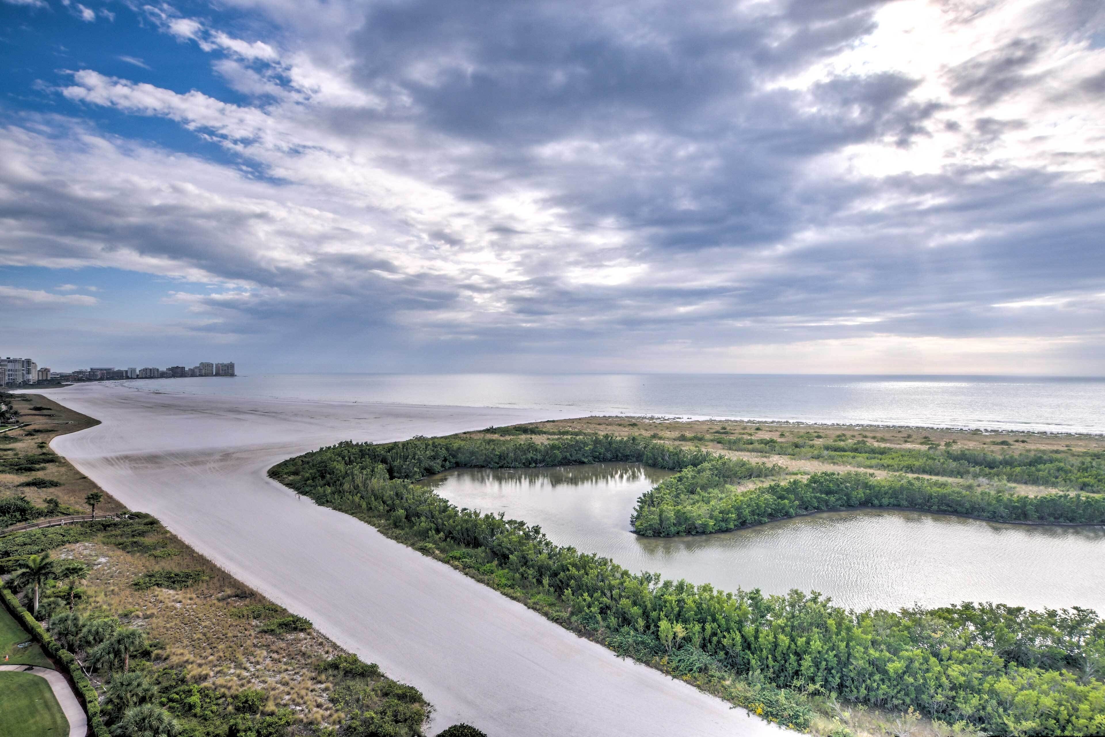 A coastal landscape with a river curving through a green area, leading to a beach.