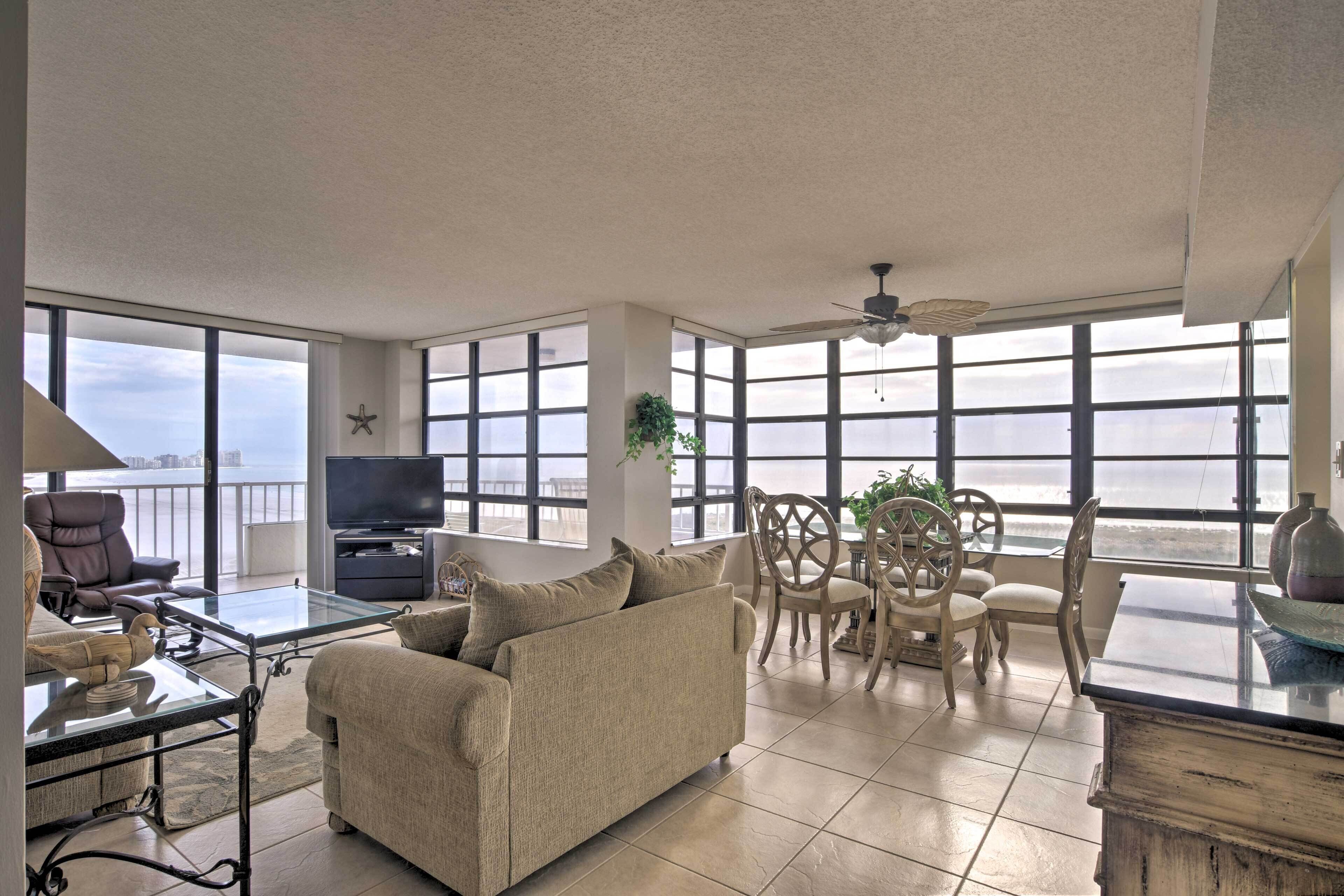 A spacious living room with a sofa, TV, and dining area by large windows overlooking a body of water.