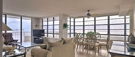 A spacious living room with a sofa, TV, and dining area by large windows overlooking a body of water.