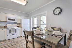 A modern kitchen with white appliances, a dining table set with plates and glasses, and a wall clock.