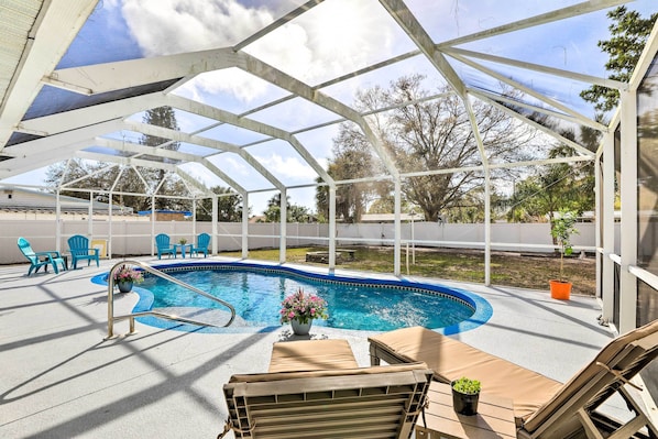 A covered outdoor swimming pool with lounge chairs and a small garden area.