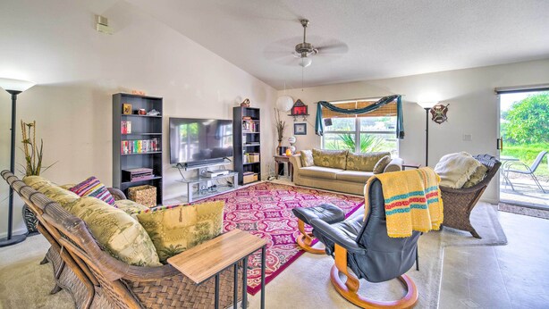 A spacious living room with a large flat-screen TV, a bookshelf, a comfortable sofa, and a dining area. - 'banzai Palm Bay' Home Near Parks & Beaches! (Palm Bay)