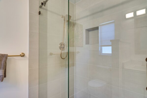 Une salle de bain moderne avec une douche à parois de verre, un porte-serviettes et une petite fenêtre.