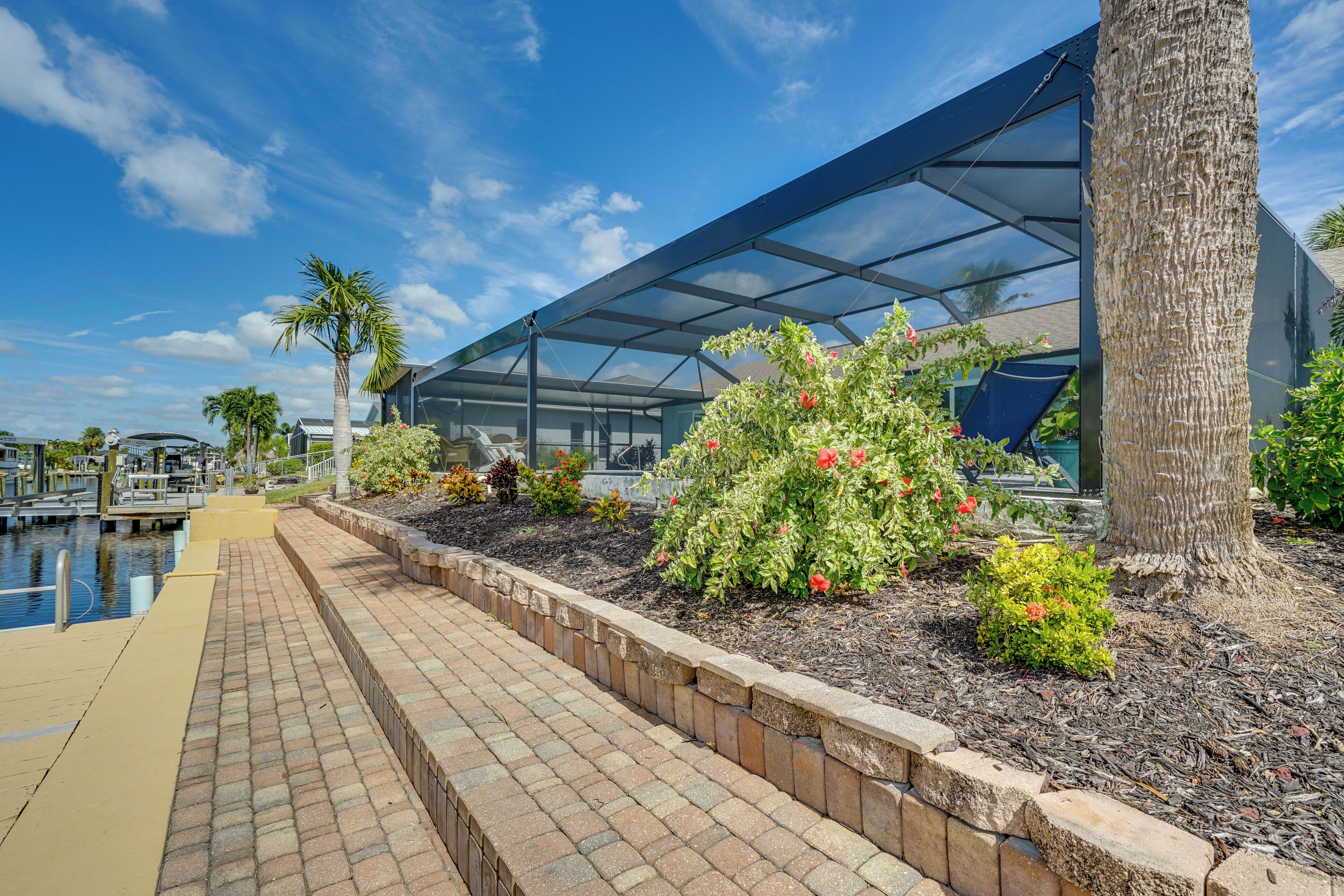 A waterfront property with a glass conservatory, a paved walkway, and landscaped gardens.