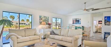 A spacious living room with two sofas, a coffee table, and large windows offering a view of a swimming pool and palm trees.