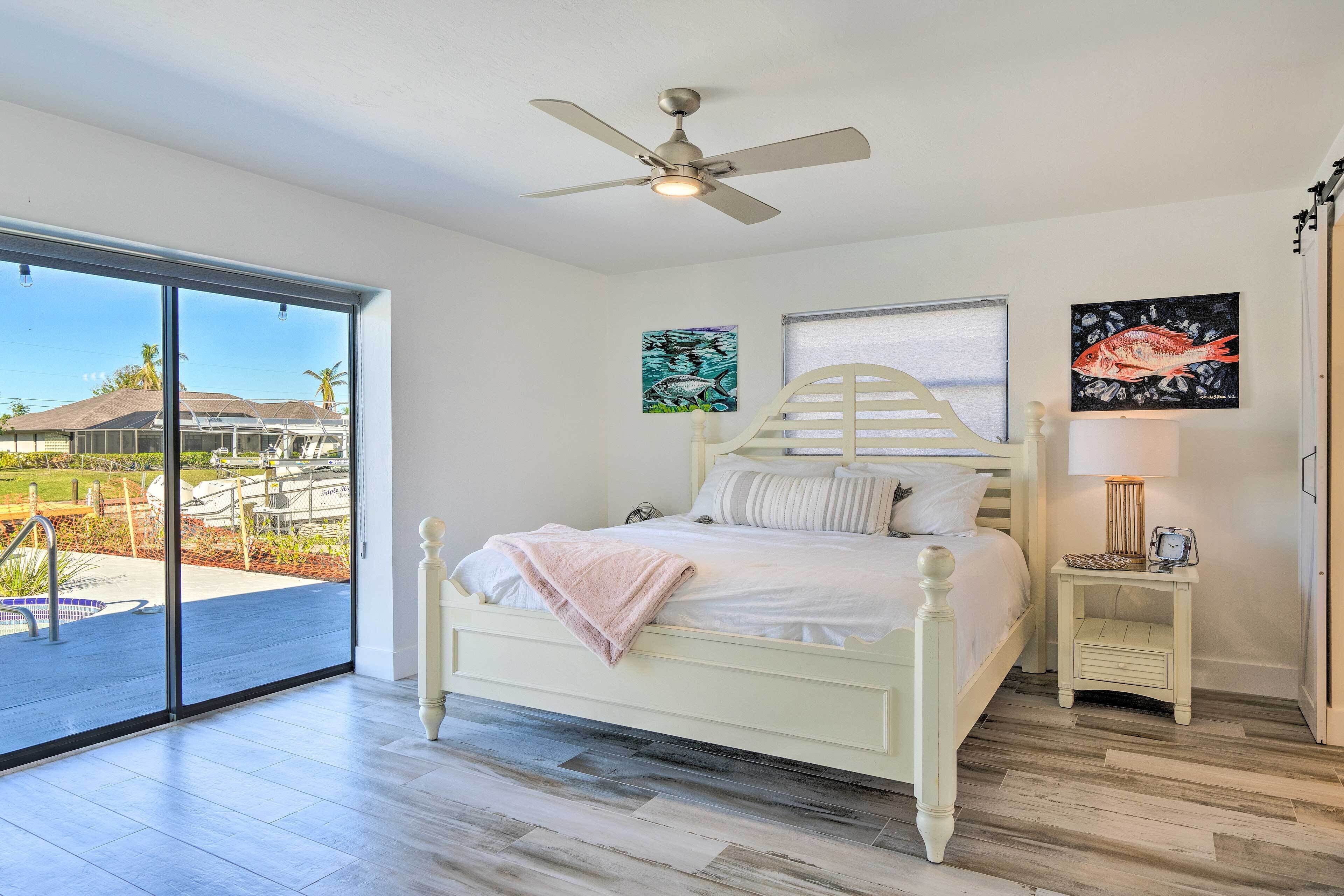 A bedroom with a bed, a ceiling fan, a nightstand, and artwork on the walls.