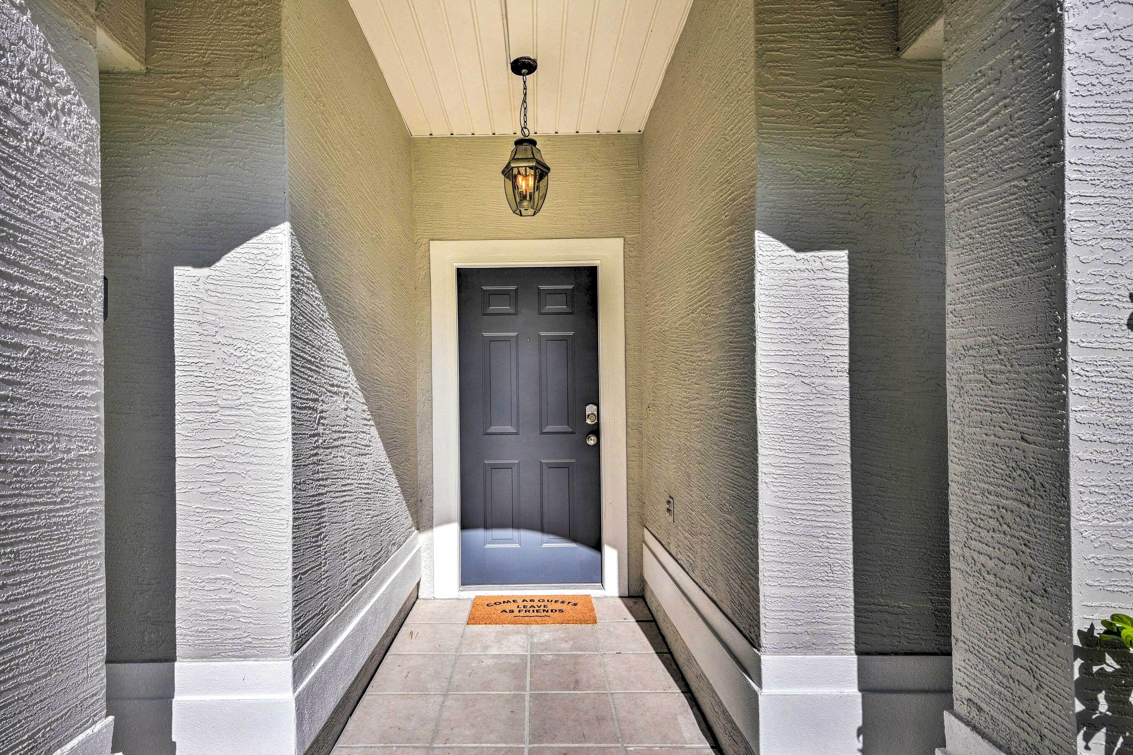 A hallway with textured walls, a dark door, and a hanging light fixture.