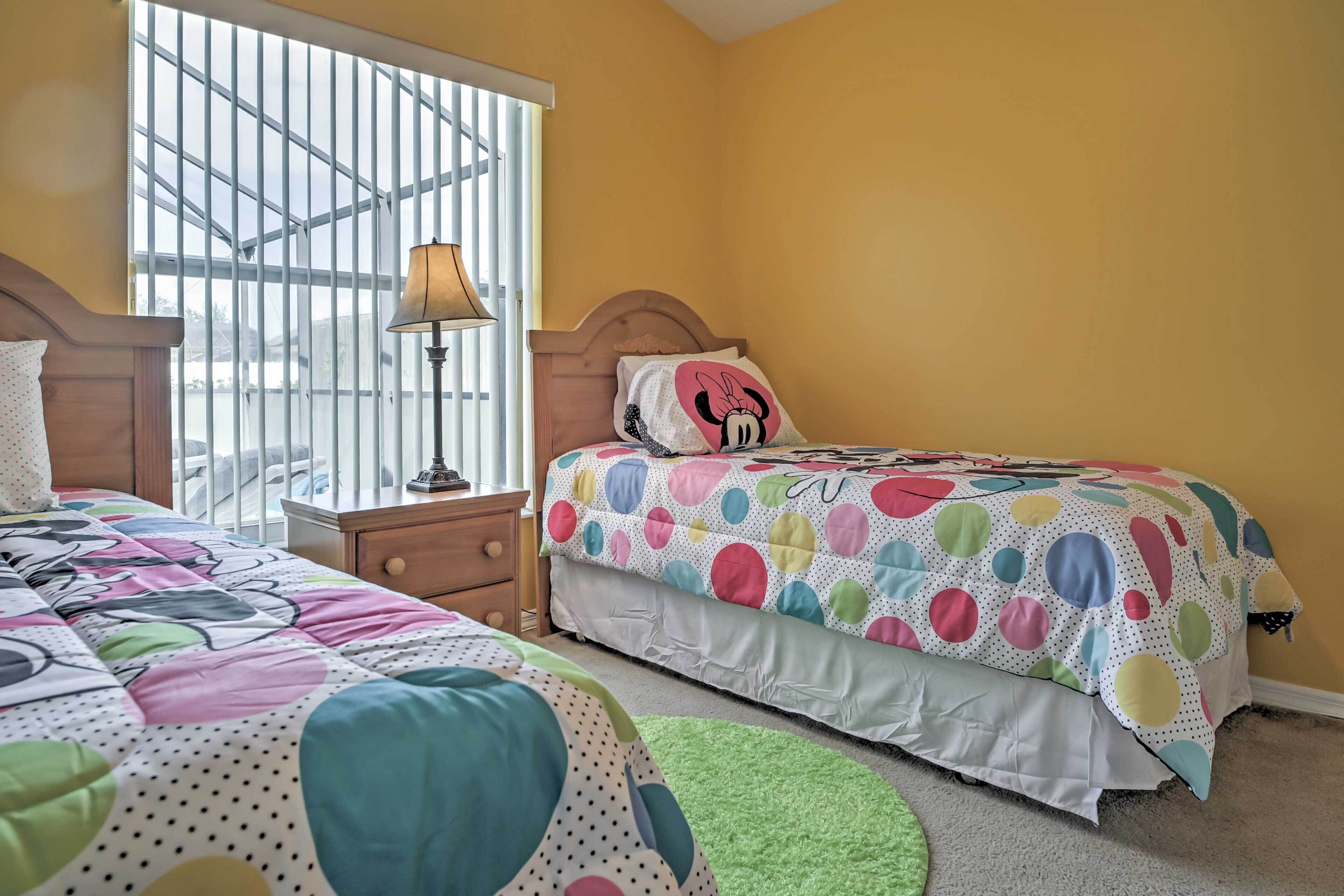 Quarto com duas camas, uma janela com persianas, uma luminária e uma almofada do Mickey Mouse.