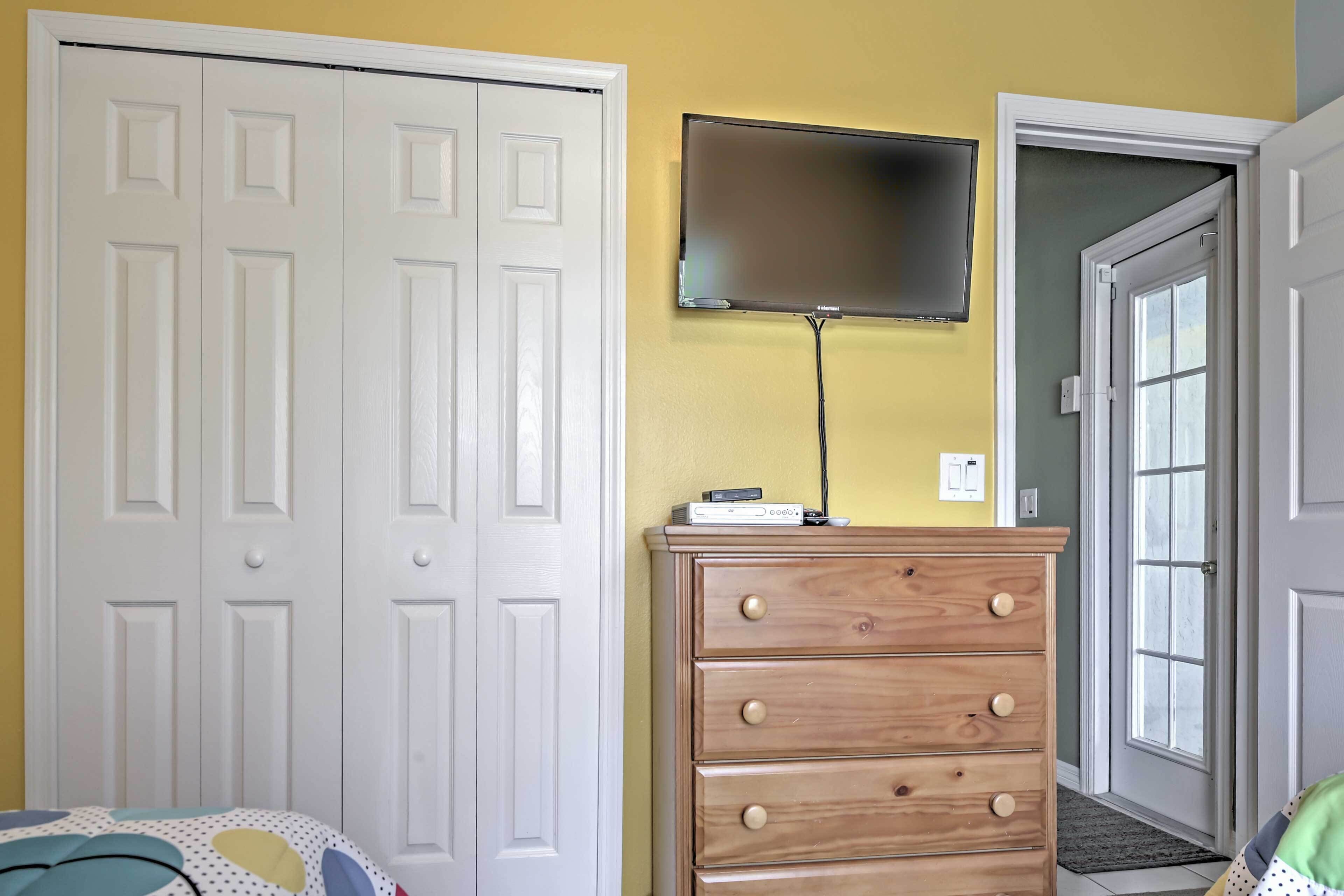 A bedroom with a white wardrobe, a wooden dresser, and a flat-screen TV mounted on the wall.