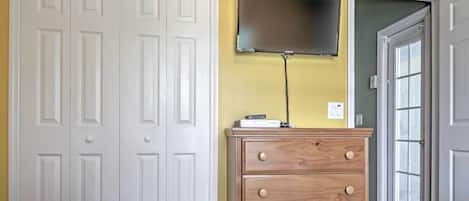 A bedroom with a white wardrobe, a wooden dresser, and a flat-screen TV mounted on the wall.