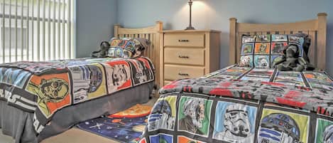 A bedroom with two beds, each with a Star Wars themed bedspread. There is a nightstand with a lamp and a drawer.