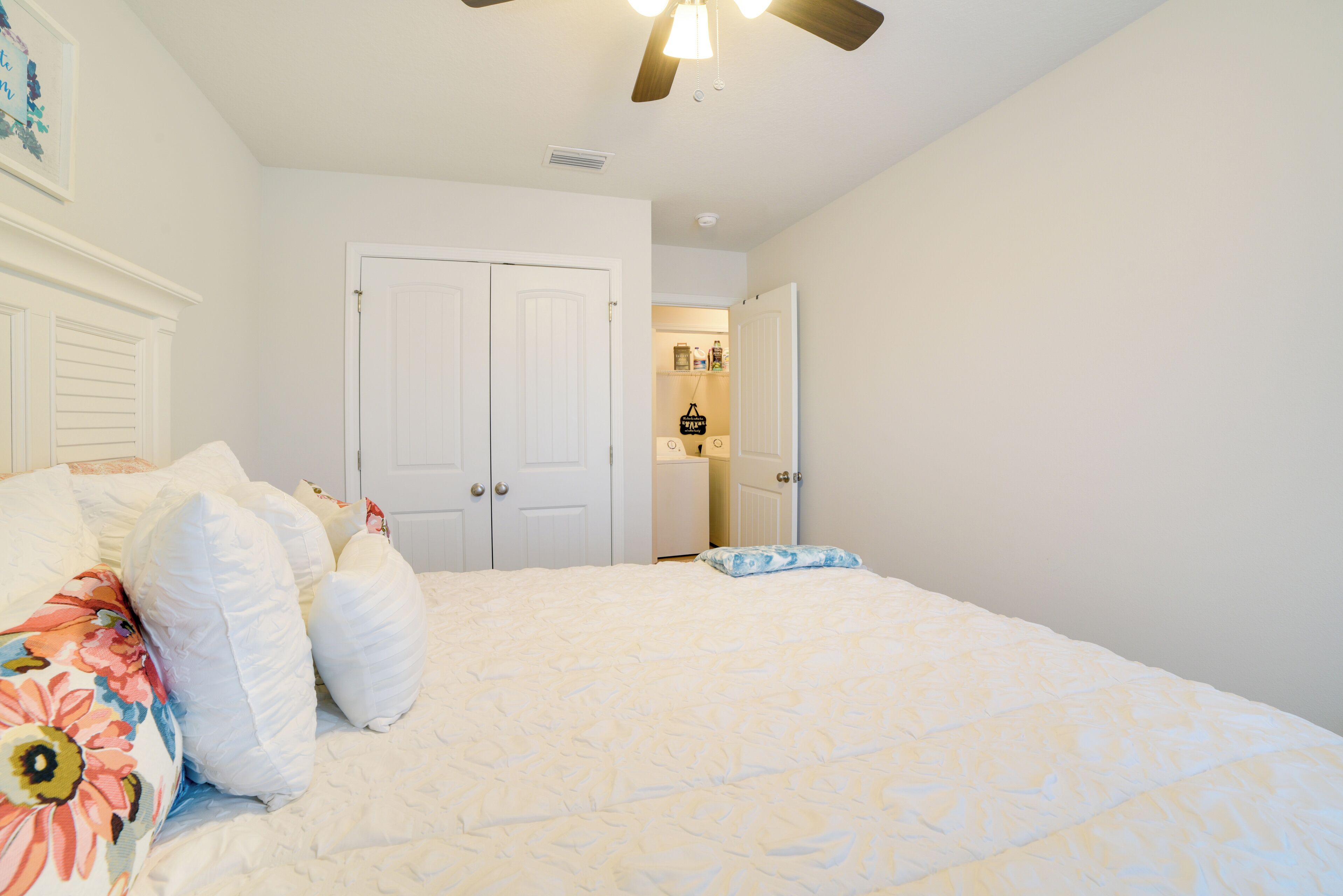 A bedroom with a bed, white walls, a ceiling fan, and a door leading to a bathroom.