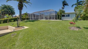Een modern huis met een grote glazen kas, omgeven door verzorgd gras en palmboompjes.