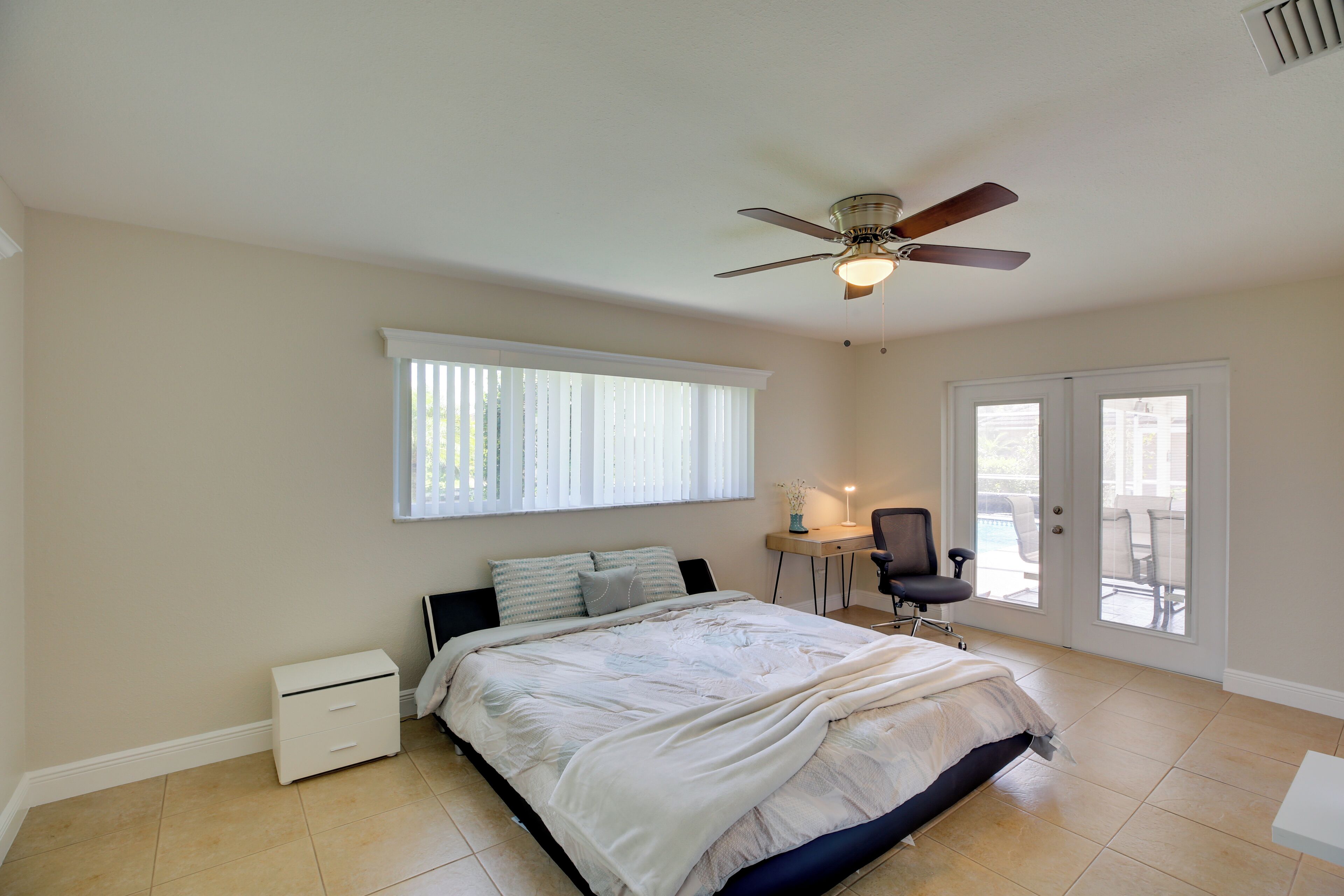 Une chambre à coucher comprenant un lit, un bureau, une chaise, un ventilateur de plafond et une porte-fenêtre coulissante.